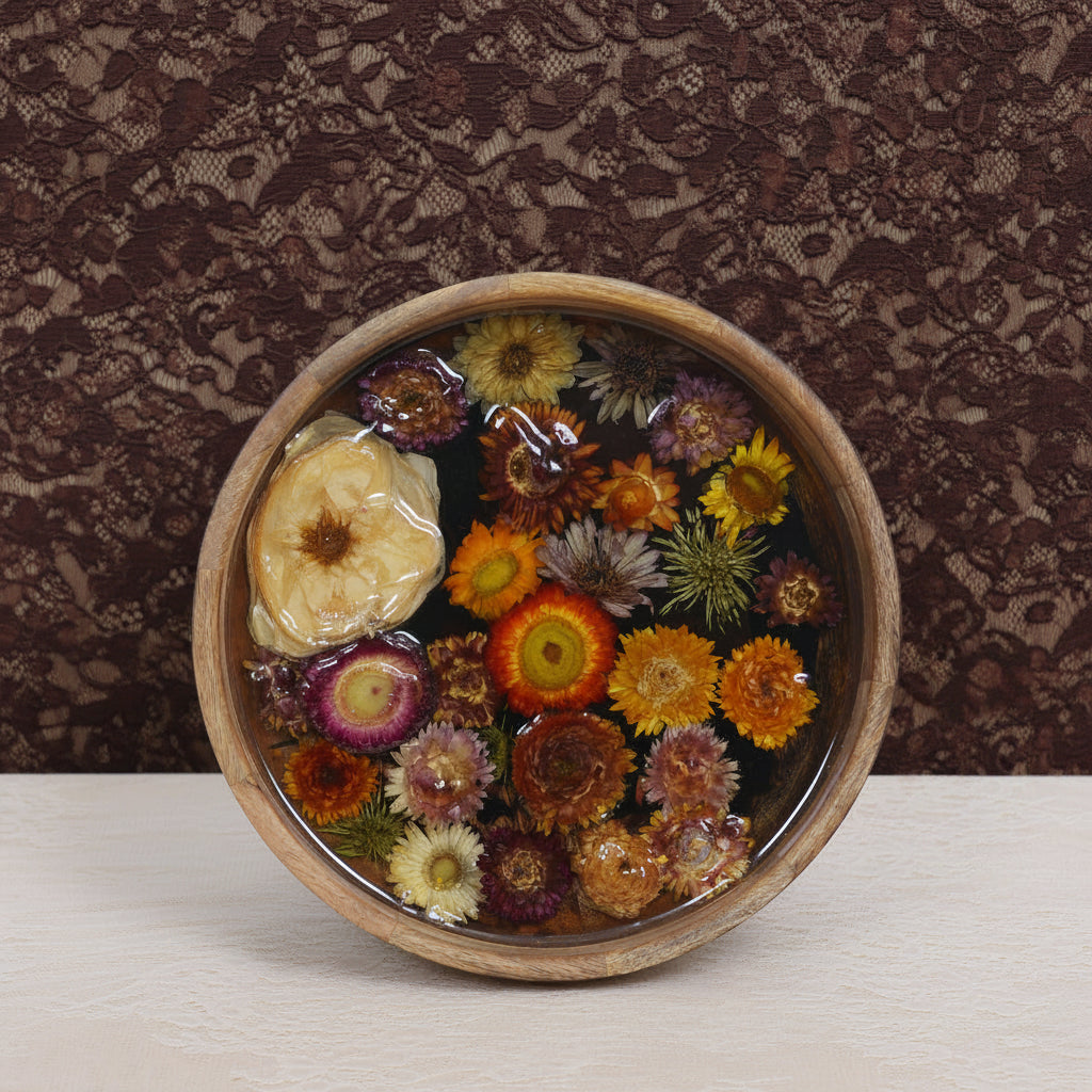 A round wooden bowl filled with preserved dried flowers under clear resin, displayed on a small stand against a light gray background.