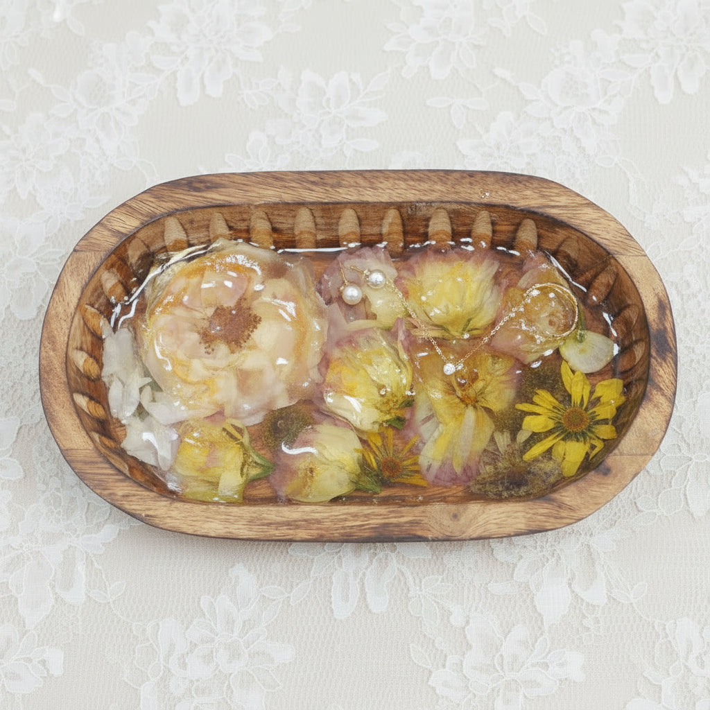 An oval mango wood tray filled with dried flowers, encased in clear glass like resin. Pearl necklace overlaying. 