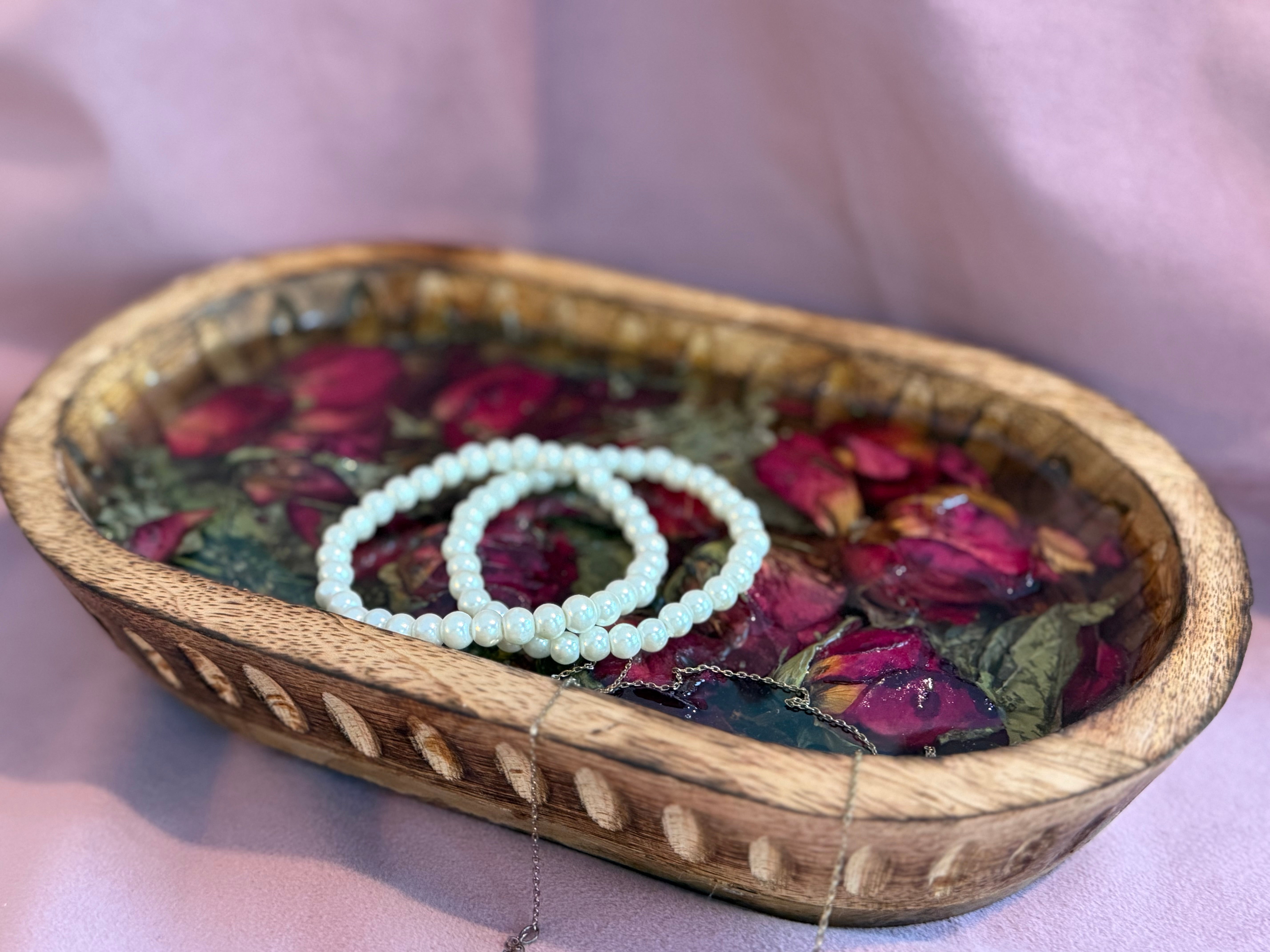 Carved wood dough bowl tray of preserved red rosebuds in resin holding two pearl bracelets and a silver chain necklace