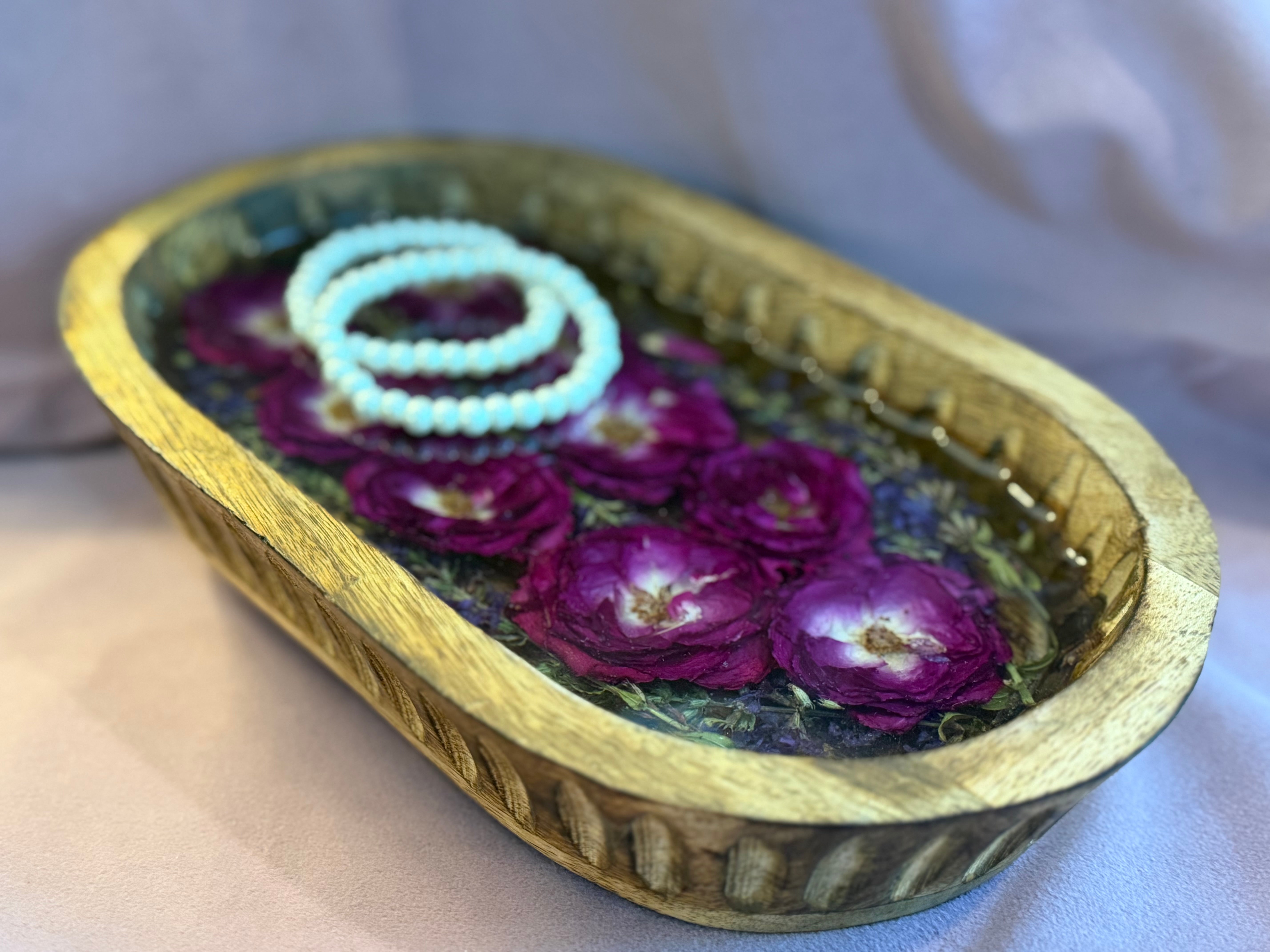 Carved wood dough bowl tray of preserved magenta roses in clear resin holding two white pearl bracelets