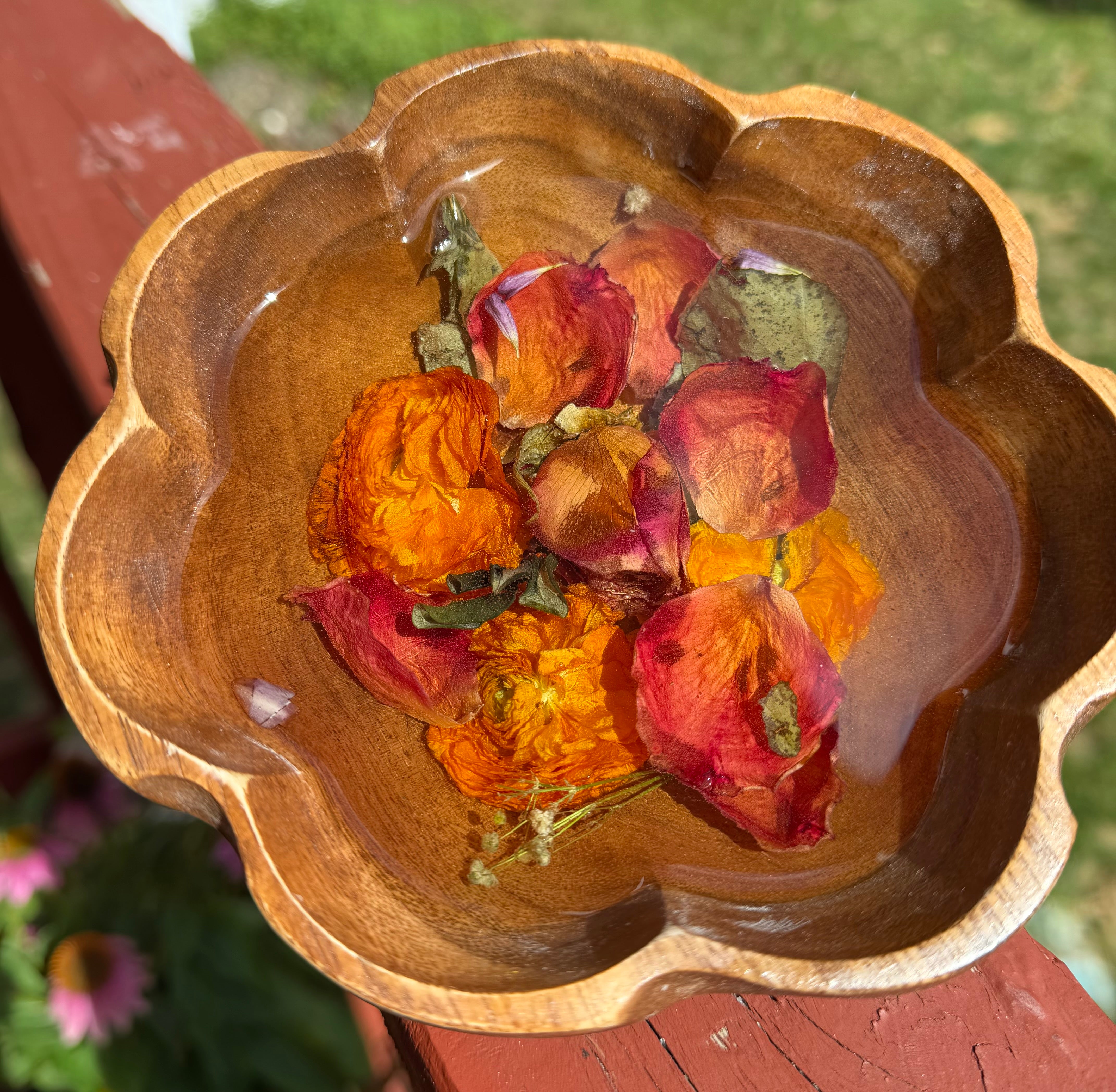 Top view of scalloped wooden bowl with preserved red and orange roses in clear resin