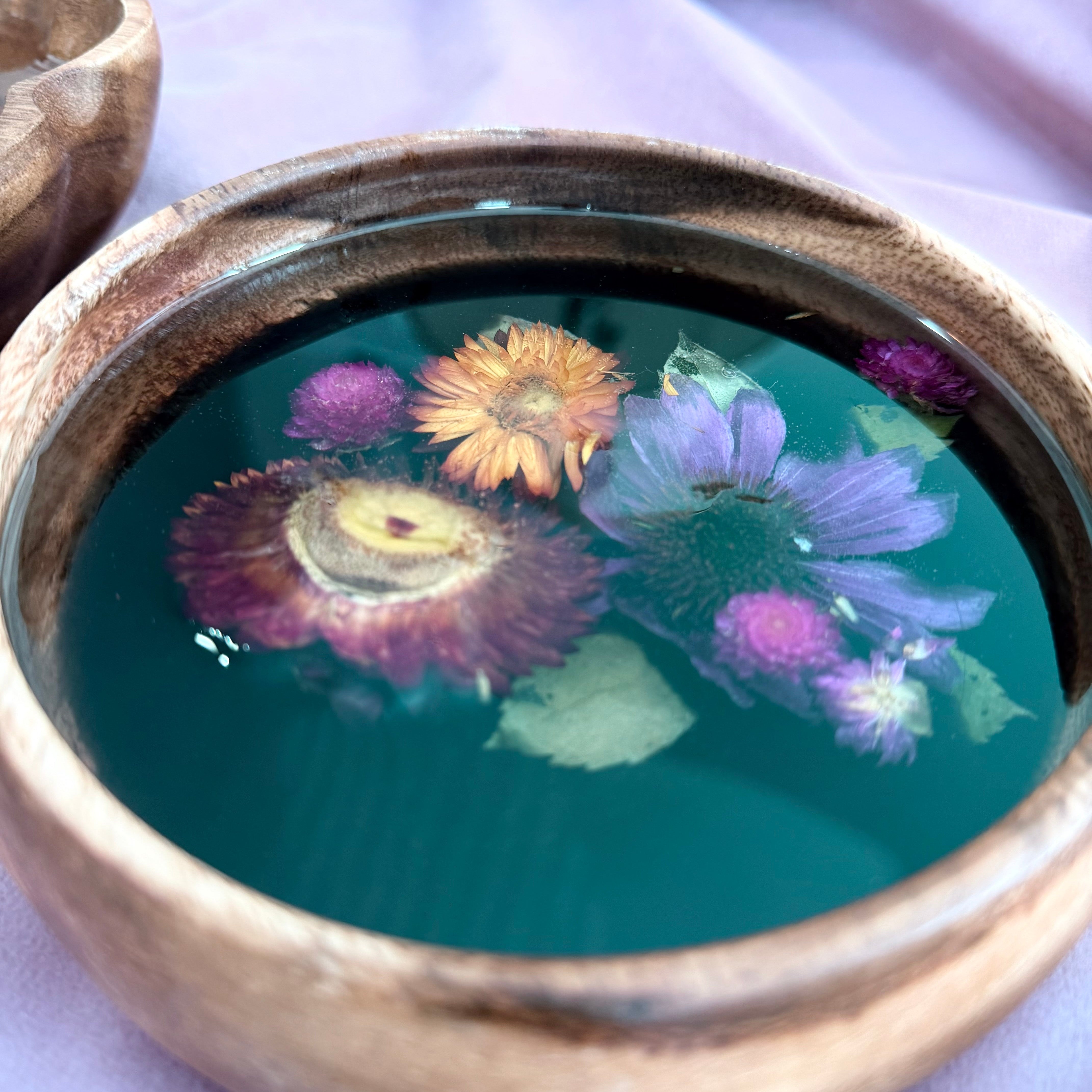 Small round wooden bowl with magenta and orange strawflowers, a purple coneflower, and purple pom-pom blooms set in black resin