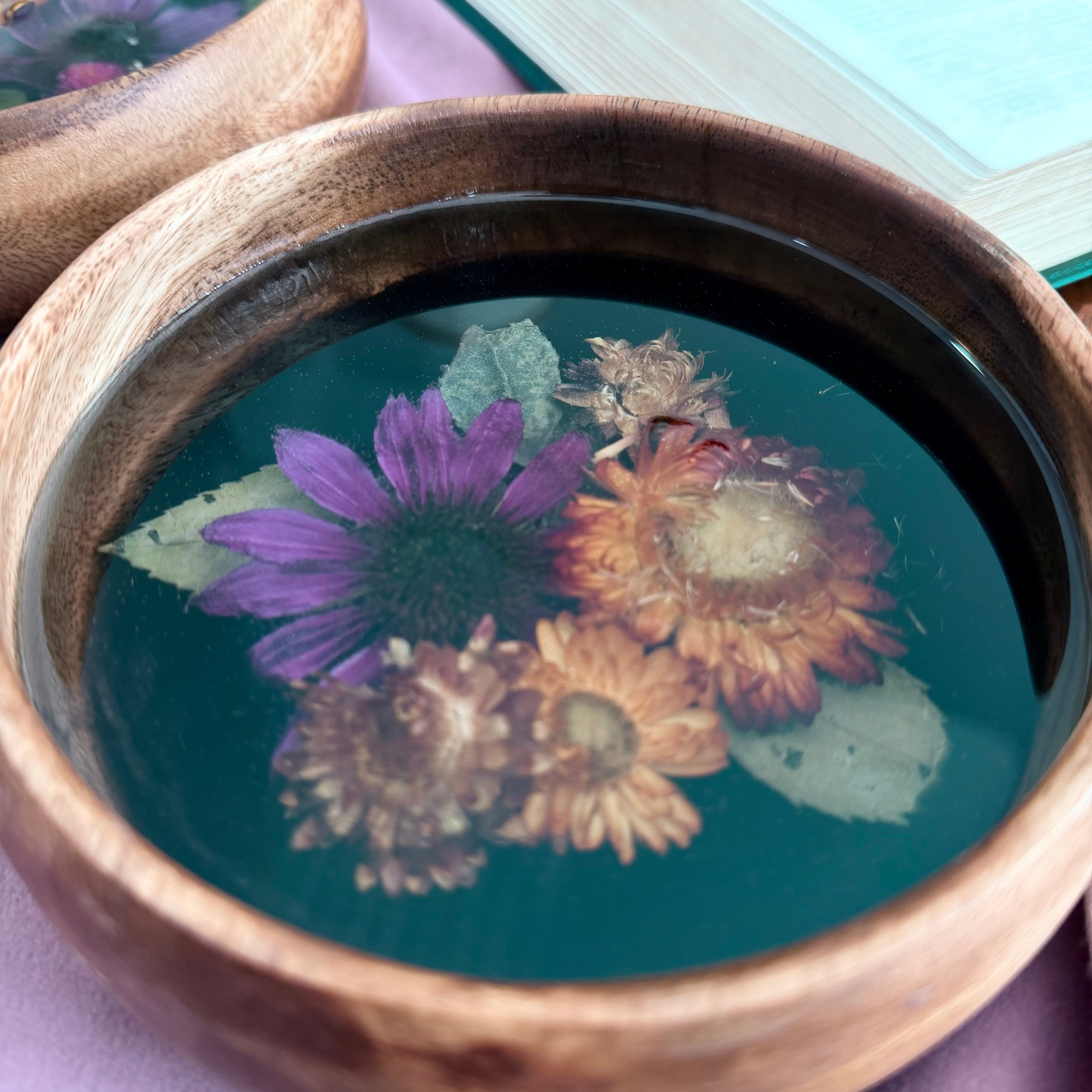 Small round wooden bowl with a purple coneflower and golden orange strawflowers set in dark resin