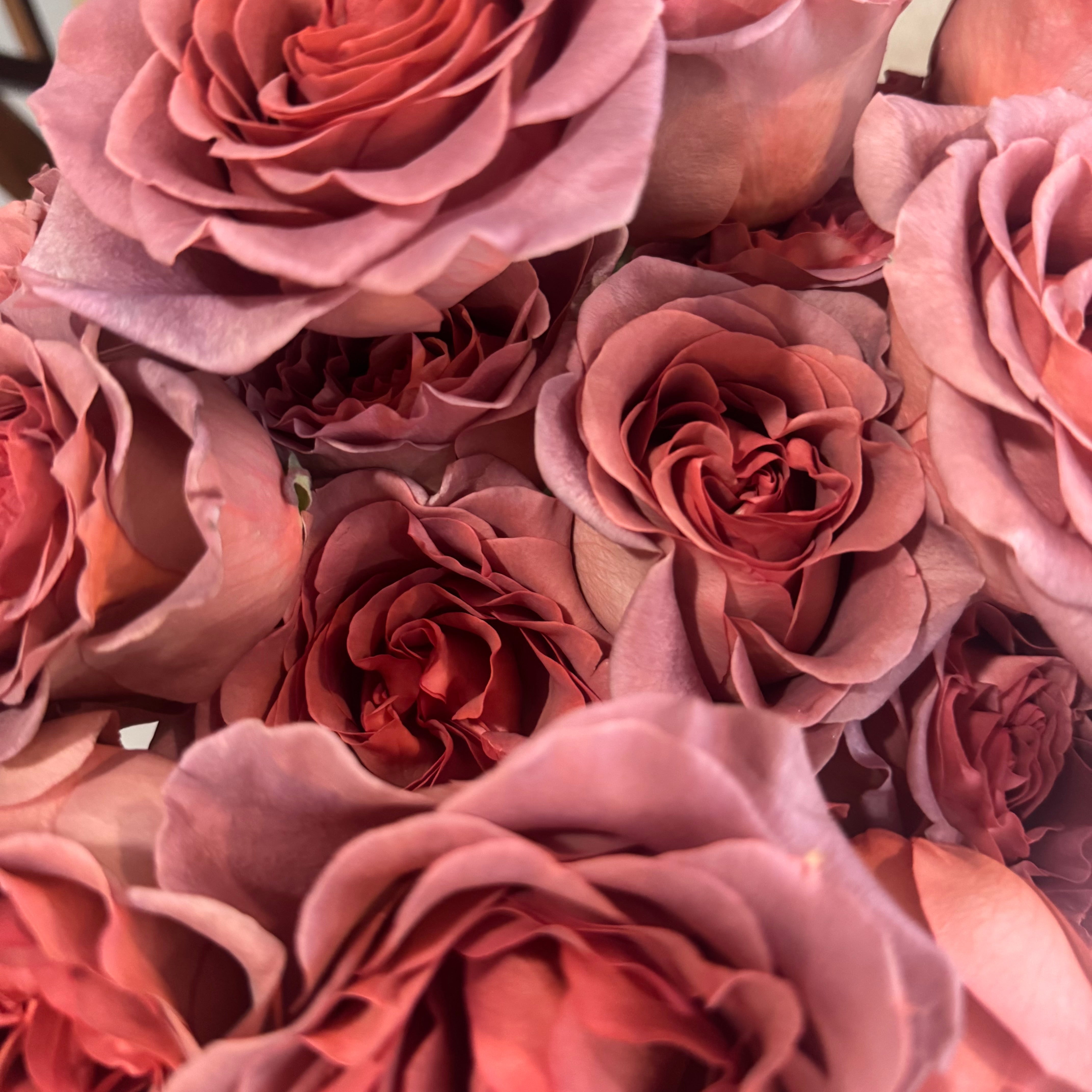 A close-up of dusty rose artificial roses with layered petals, filling the entire frame.