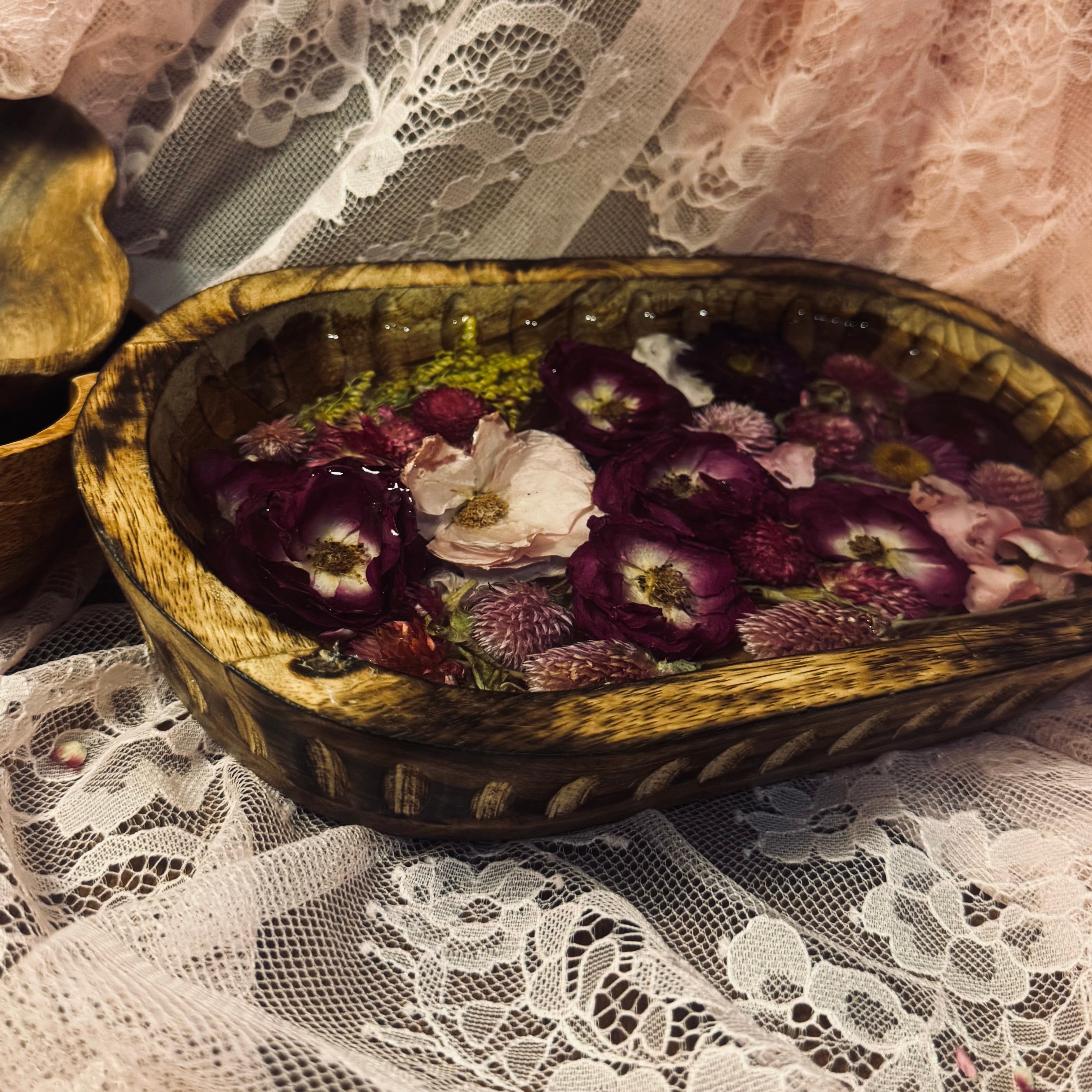 Mango wood oval keepsake bowl with purple and pink preserved roses and goldenrod set in resin, styled on white and pink lace with a small vintage shell nearby