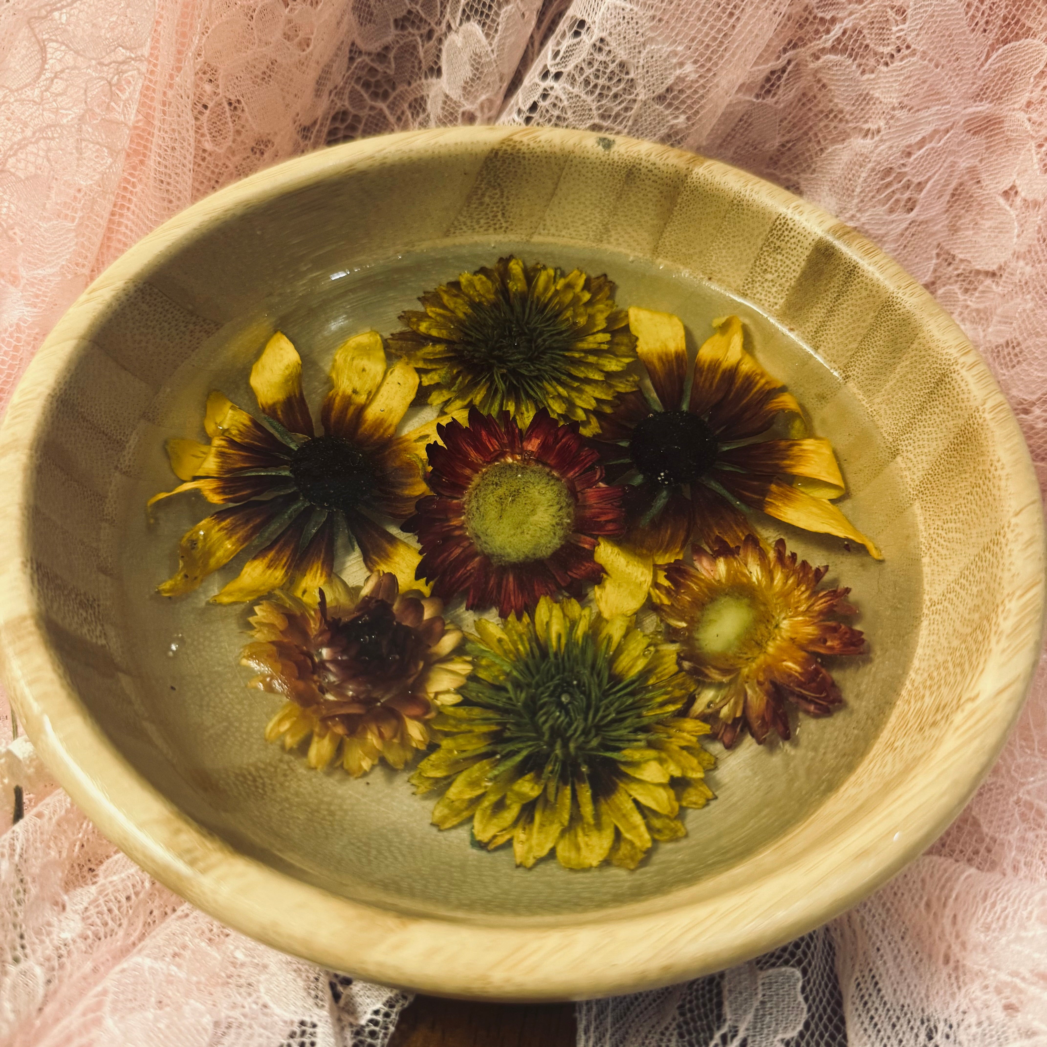 Round bamboo bowl filled with golden and burgundy strawflowers set in clear resin, styled on pink lace fabric