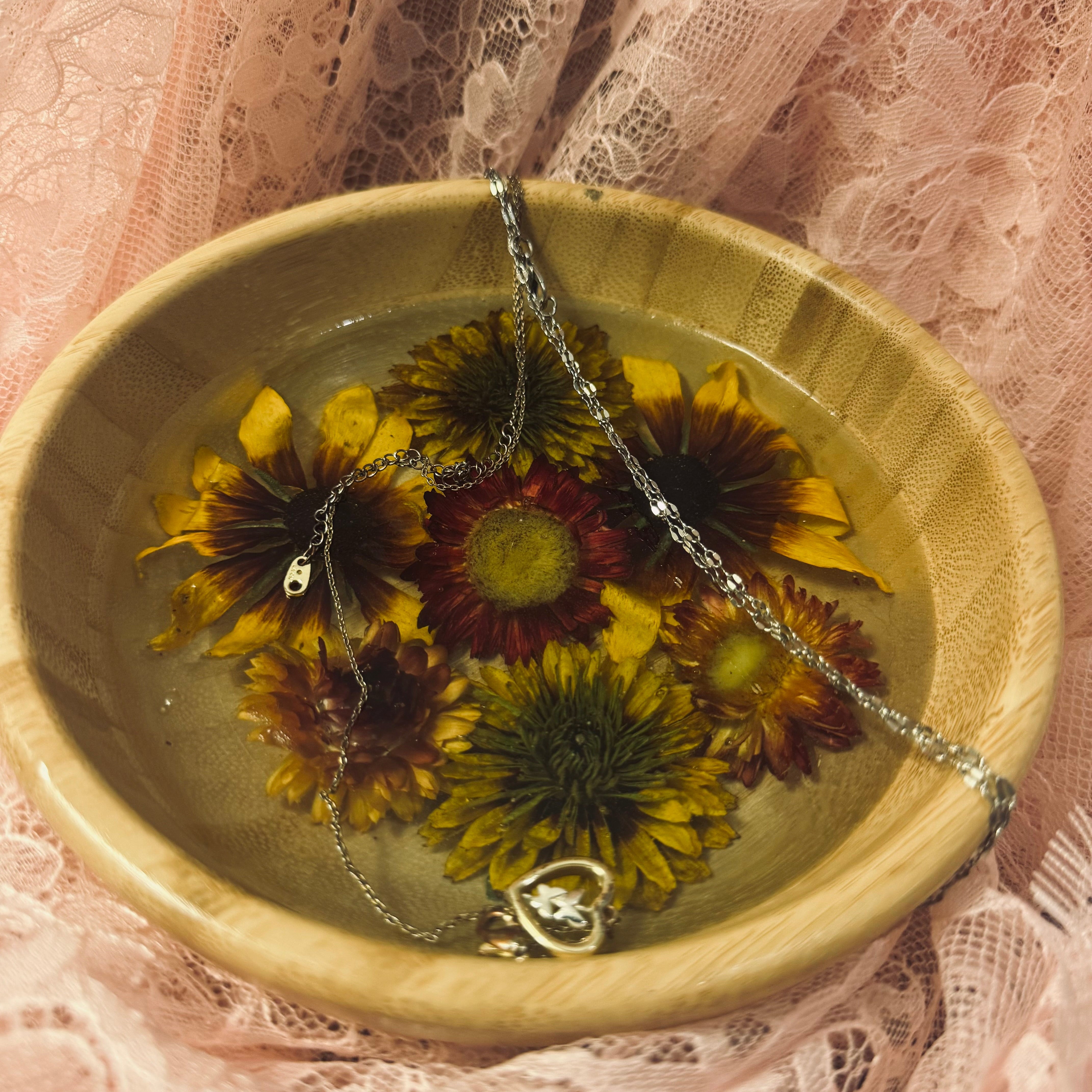 Round bamboo bowl with golden and burgundy strawflowers set in clear resin, styled with a silver necklace on pink lace fabric