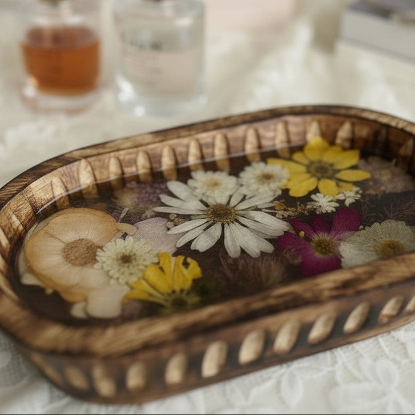 An oval wooden tray filled with dried flowers and botanicals, placed on a white surface in front of a white cabinet with a black knob.